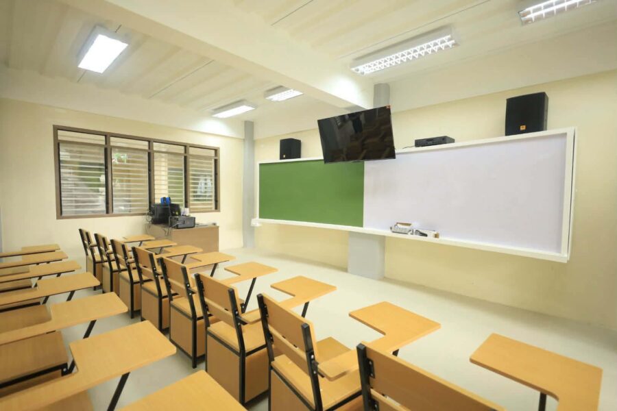 Modern smart classroom featuring a PC, LED TV, and ceiling-mounted projector with integrated speakers and microphone.
