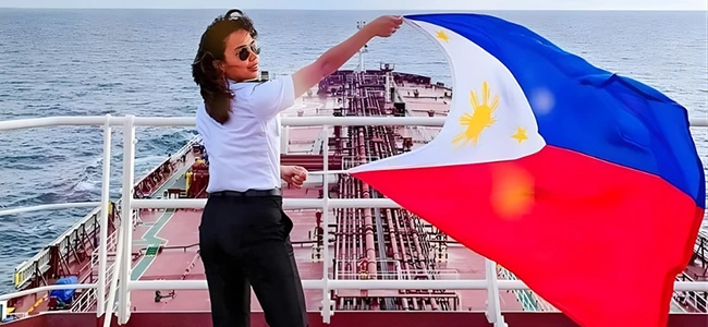 Second Officer KC Abigail Chin-Sood, a pioneering Mindanaoan seafarer, stands on the bridge deck of an international tanker vessel, confidently waving the Philippine flag to symbolize her successful 12-year career and the growing presence of Filipino women in maritime leadership.
