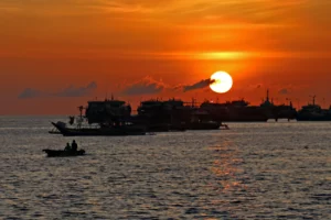 A fiery orange sunset over the bay in Zamboanga City with silhouettes of a moving fishing boat and cargo vessels on the horizon, captured on April 6, 2026.