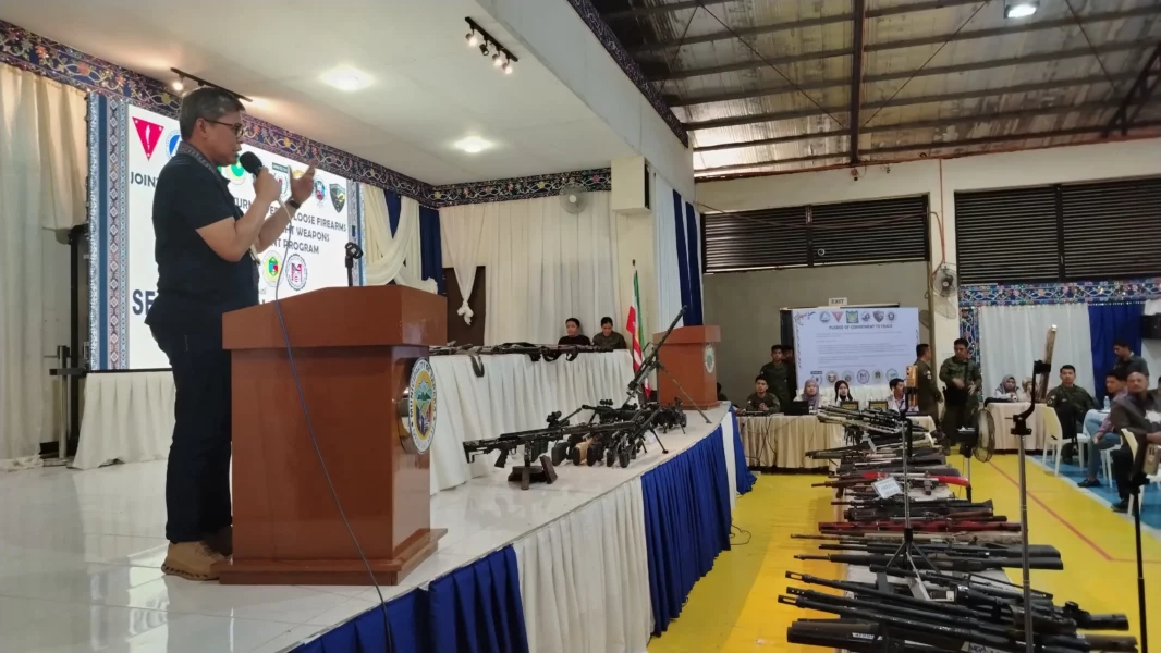 Municipal mayors and military officials standing behind rows of surrendered loose firearms during the SALW ceremony in Taraka.