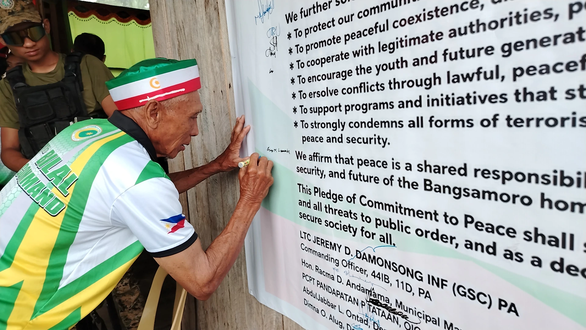 MILF Bilal Command leader wearing a green, white, and red cap signs his name on a large "Pledge of Commitment to Peace" banner.