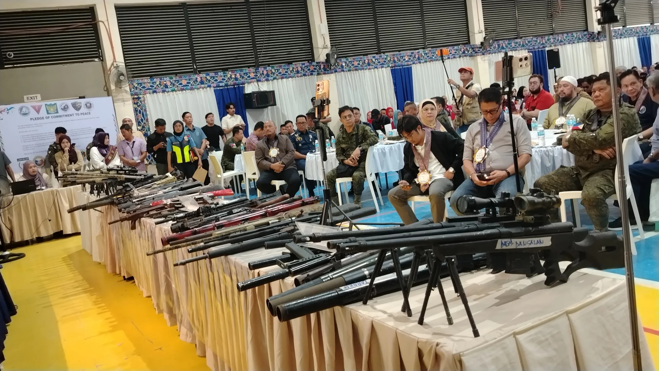 A focused, perspective shot taken down a table laden with surrendered sniper rifles, shotguns, and long-range weapons in Taraka.