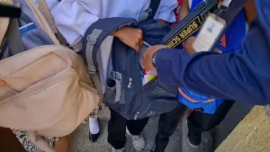 Security personnel use a handheld metal detector to conduct a non-contact electronic bag inspection at a school entrance gate.