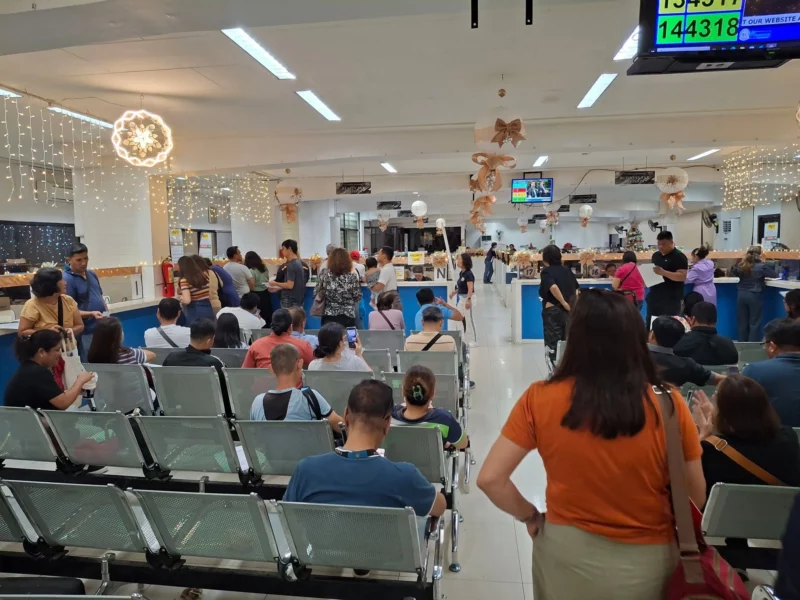 A wide indoor view of taxpayers sitting in rows of metal chairs and queuing at service counters under decorative lights inside the Cagayan de Oro City Treasurer's Office.