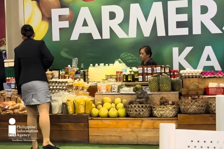 A shopper examines fresh vegetables and agricultural goods displayed at a Department of Agriculture Kadiwa pop-up market stall inside a shopping mall corridor.