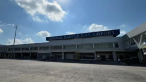 The exterior facade of the General Santos City Airport terminal building under a clear blue sky, showing the main entrance areas empty during a temporary post-earthquake closure.