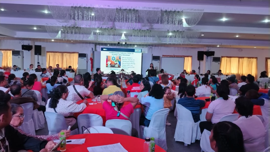 A large group of local residents and government officials sit in rows of chairs during an institutional seminar inside a well-lit function hall.
