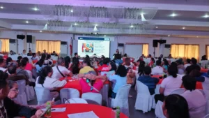 A large group of local residents and government officials sit in rows of chairs during an institutional seminar inside a well-lit function hall.
