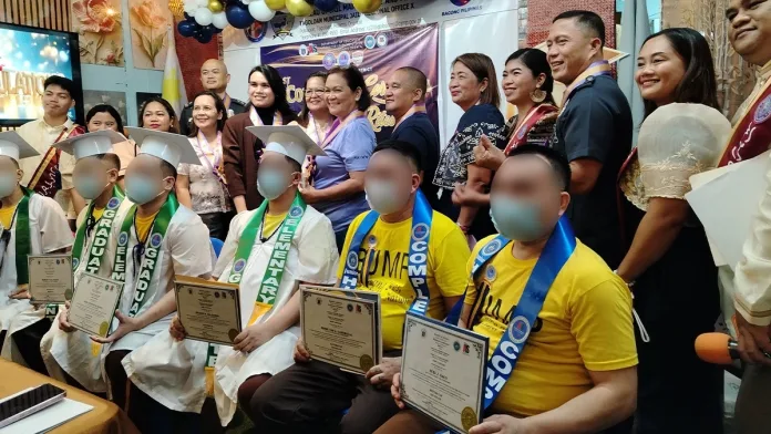 Six persons deprived of liberty smile and celebrate while holding their Alternative Learning System diplomas inside the BJMP Tagoloan facility.