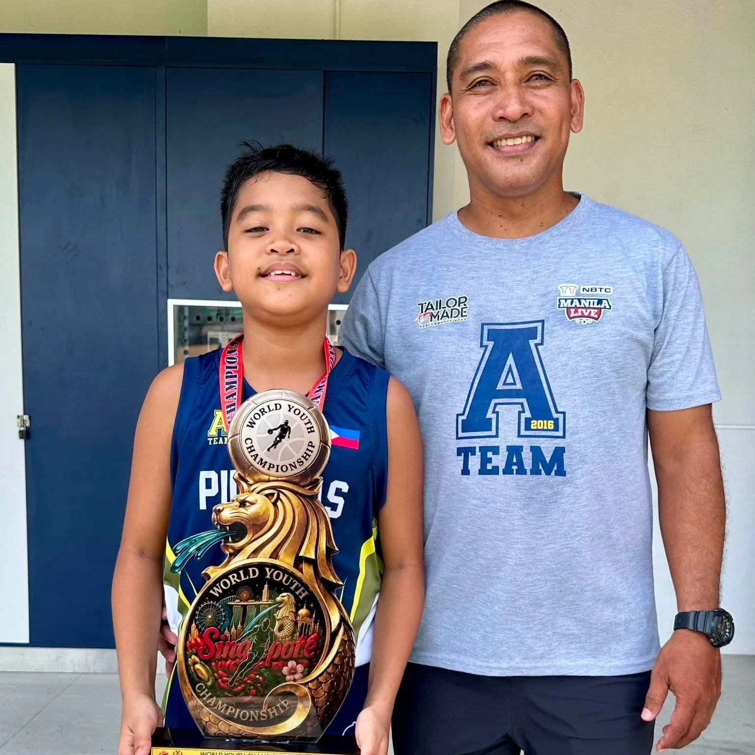 TRIUMPH OVER ADVERSITY: Head coach Arvin Martinez, right, stands alongside his son and starting guard, Leba Deomidi “LD” Martinez, as LD holds the U11 World Youth Championship trophy following A-Team Pilipinas' gold-medal victory in Singapore in August 2026. LD recovered from emergency surgery weeks before departure to help the Cagayan de Oro-based team sweep the tournament. (Photo courtesy of Philippine Youth Dreamers Org.)