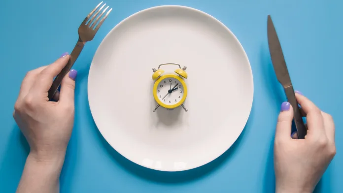 A conceptual arrangement shows an alarm clock centered on an empty dinner plate, representing the meal-skipping patterns adopted by young professionals and students. Health experts warn that restricting food intake without proper nutrition may not meet varying dietary needs, even as rising costs for fresh produce and protein force young consumers toward cheaper alternatives or fewer meals altogether.