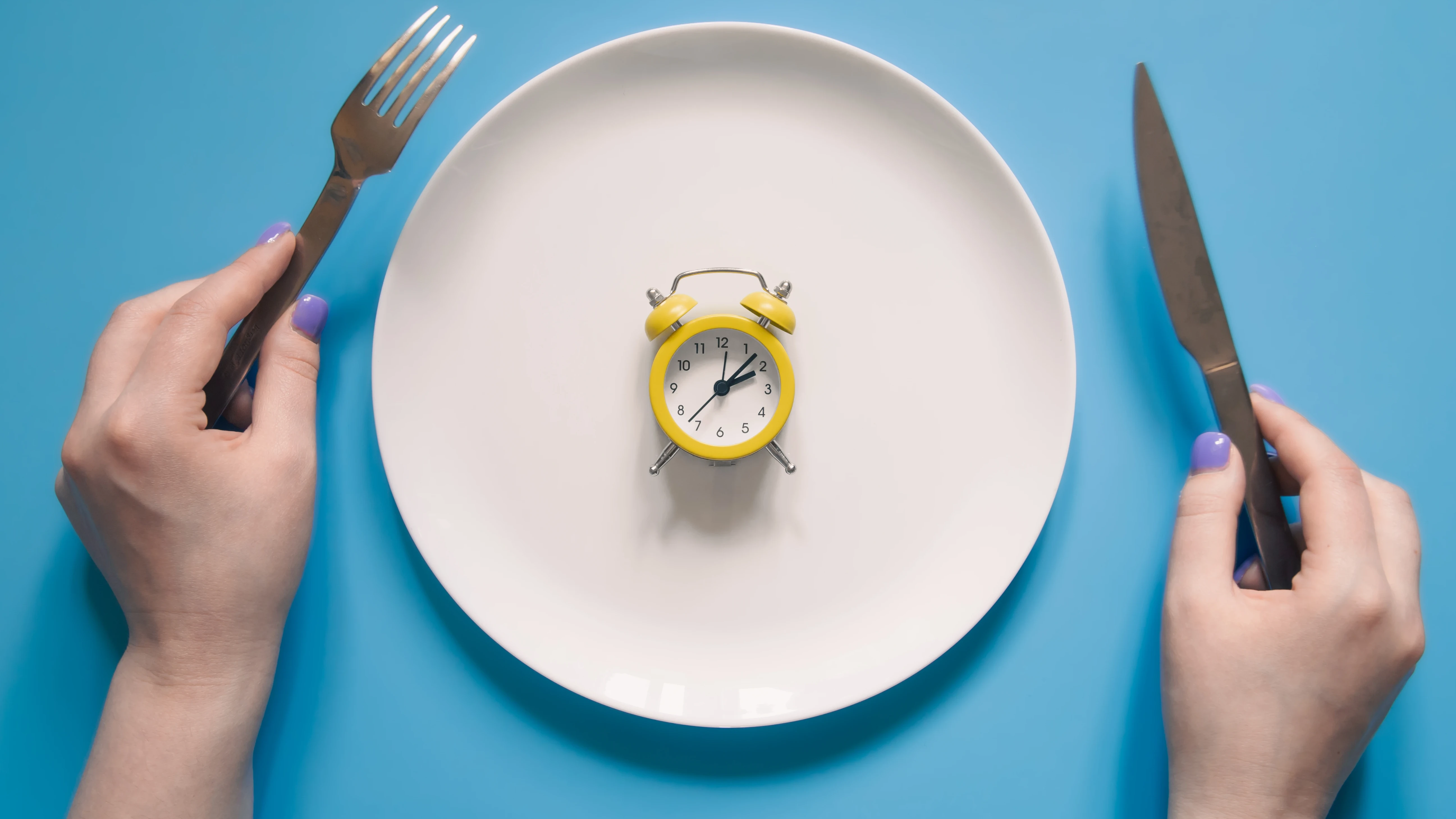 A conceptual arrangement shows an alarm clock centered on an empty dinner plate, representing the meal-skipping patterns adopted by young professionals and students. Health experts warn that restricting food intake without proper nutrition may not meet varying dietary needs, even as rising costs for fresh produce and protein force young consumers toward cheaper alternatives or fewer meals altogether.