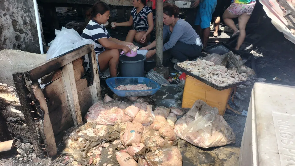 SALVAGING LIVELIHOODS: Displaced vendors sit amid soot and debris, attempting to clean and recover raw poultry inventory following a third-alarm fire at EEDMO Building C inside the Iligan Central Public Market on Aug. 23. The blaze destroyed stock and equipment for 167 stall owners, prompting urgent appeals for immediate capital support and temporary relocation sites. (Photo by Bonita L. Ermac)