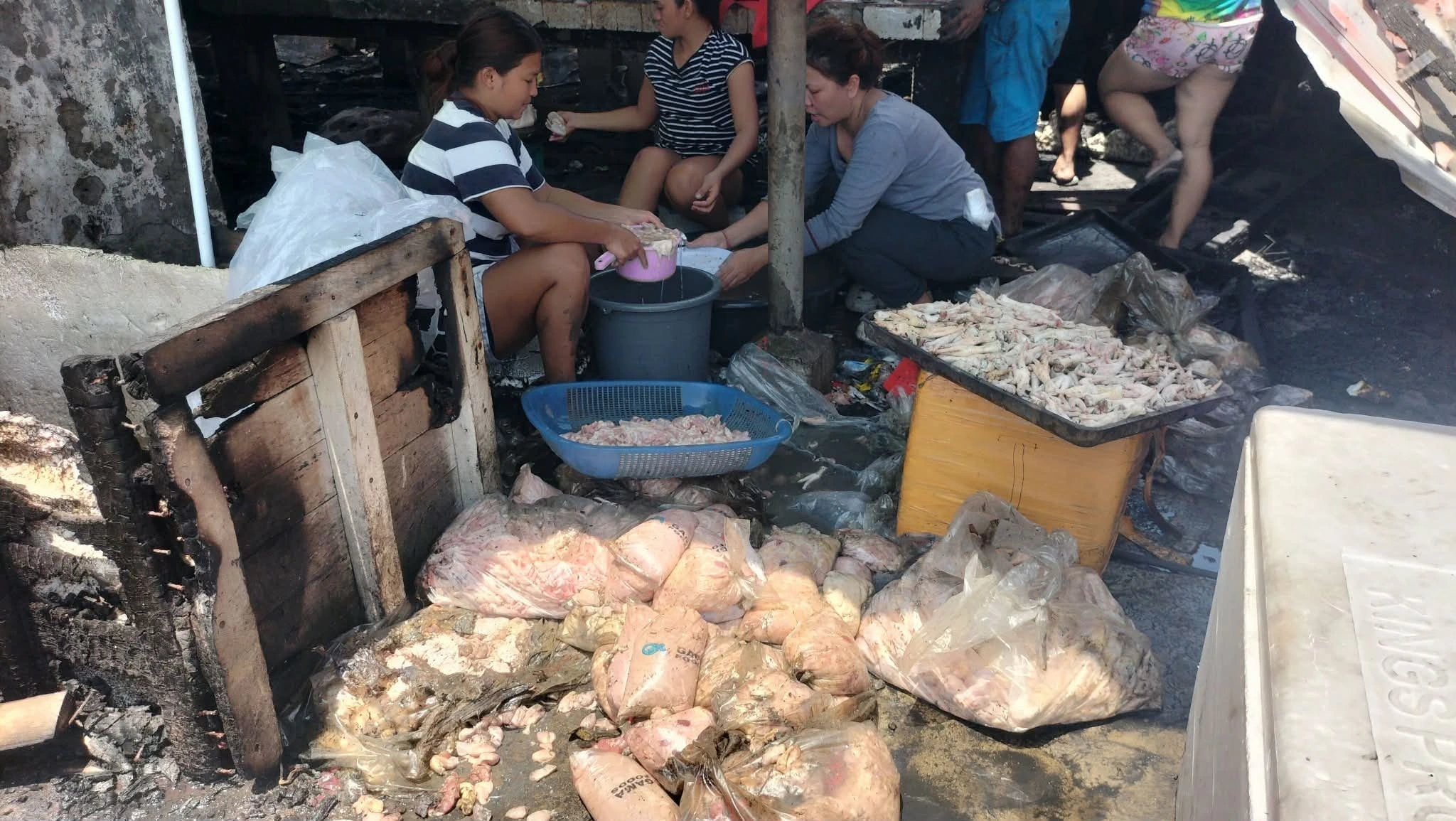 SALVAGING LIVELIHOODS: Displaced vendors sit amid soot and debris, attempting to clean and recover raw poultry inventory following a third-alarm fire at EEDMO Building C inside the Iligan Central Public Market on Aug. 23. The blaze destroyed stock and equipment for 167 stall owners, prompting urgent appeals for immediate capital support and temporary relocation sites. (Photo by Bonita L. Ermac)