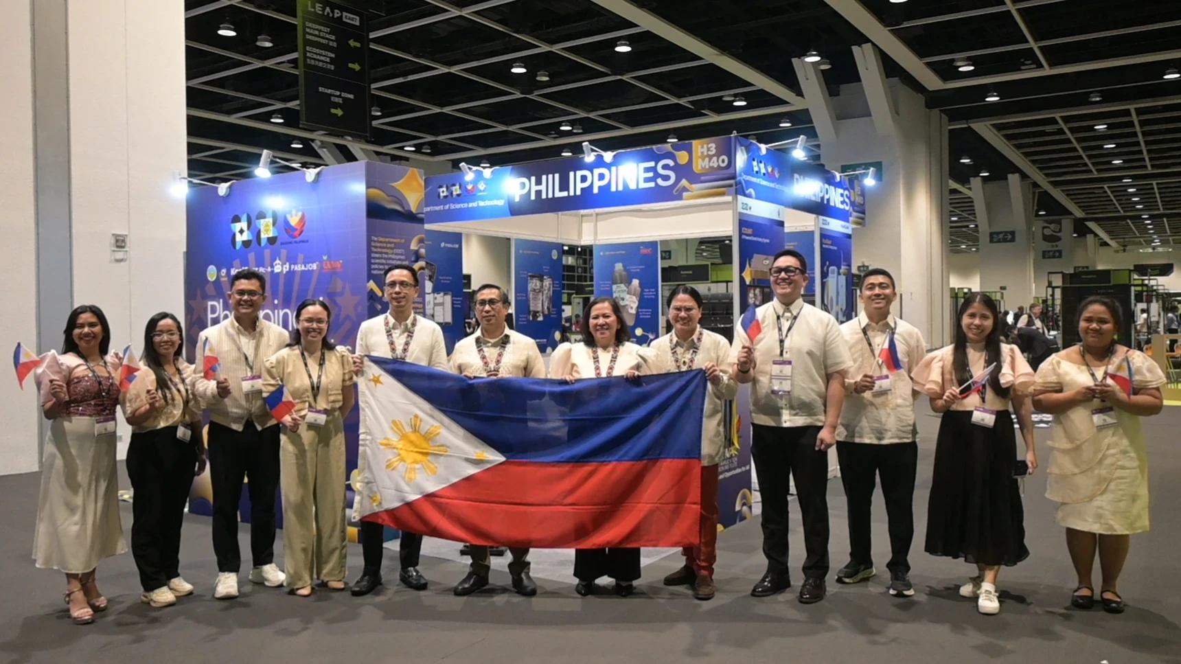 Members of the Philippine delegation, led by the Department of Science and Technology-Technology Application and Promotion Institute (DOST-TAPI) and Consul General Romulo Victor Israel Jr., hold the Philippine flag in front of the country's pavilion during LEAP East Hong Kong 2026 on Monday, August 3, 2026. Davao City-based startup Pic-A-Talk was featured alongside five other Philippine innovations at the inaugural technology expo. (Photo courtesy of DOST-TAPI)
