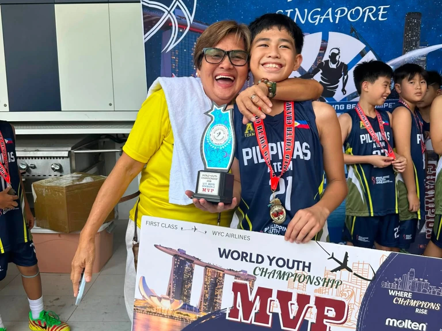 FAMILY PRIDE: Tournament Most Valuable Player Rafael Peja Cabusca Reyes, right, celebrates with his grandmother, left, while holding his U11 Division 2 MVP trophy and commemorative board in Singapore in August 2026. Reyes led the Cagayan de Oro-based A-Team Pilipinas to a tournament sweep at the 3rd World Youth Championship, defeating host Singapore Basketball Academy in the final. (Photo courtesy of A-Team Basketball Program)
