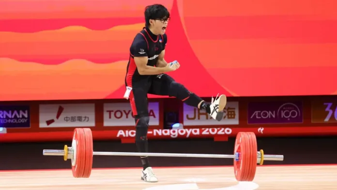 Philippine weightlifter Albert Ian delos Santos reacts with a passionate shout, kick, and clenched fists after completing a successful lift with a heavy barbell resting on the platform behind him.