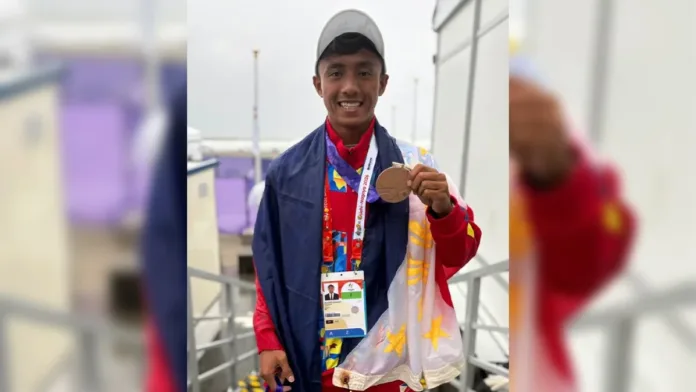 Filipino surfer Jayuard Alciso smiling while draped in the Philippine flag and holding up his Asian Games bronze medal.