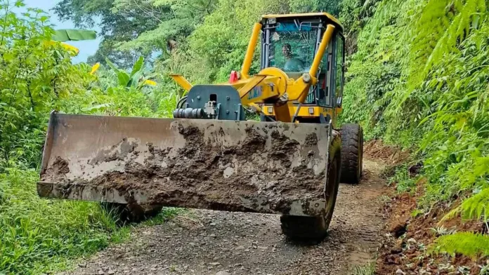 Heavy road grader equipment clearing and leveling a muddy unpaved mountain road connecting Sitio Lantad in Barangay Kibanban, Balingasag, Misamis Oriental.