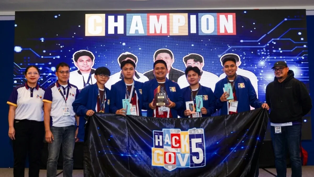Members of MSU-IIT's Team CYB3RUS hold a trophy and a banner reading "HackForGov 5" while posing on stage with event organizers in front of a digital screen displaying "CHAMPION".