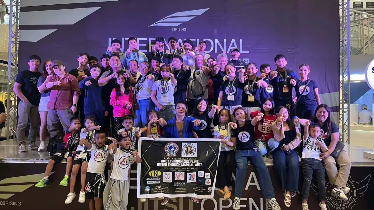 Members, youth athletes, and coaches of the Ricardo Cavalcanti Brazilian Jiu-Jitsu (RCBJJ) Team Brooks posing on stage while holding their medals and displaying their team banner following their championship win in Davao City.