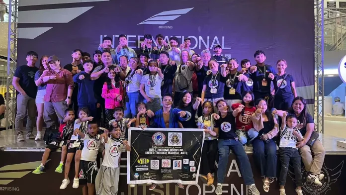Members, youth athletes, and coaches of the Ricardo Cavalcanti Brazilian Jiu-Jitsu (RCBJJ) Team Brooks posing on stage while holding their medals and displaying their team banner following their championship win in Davao City.