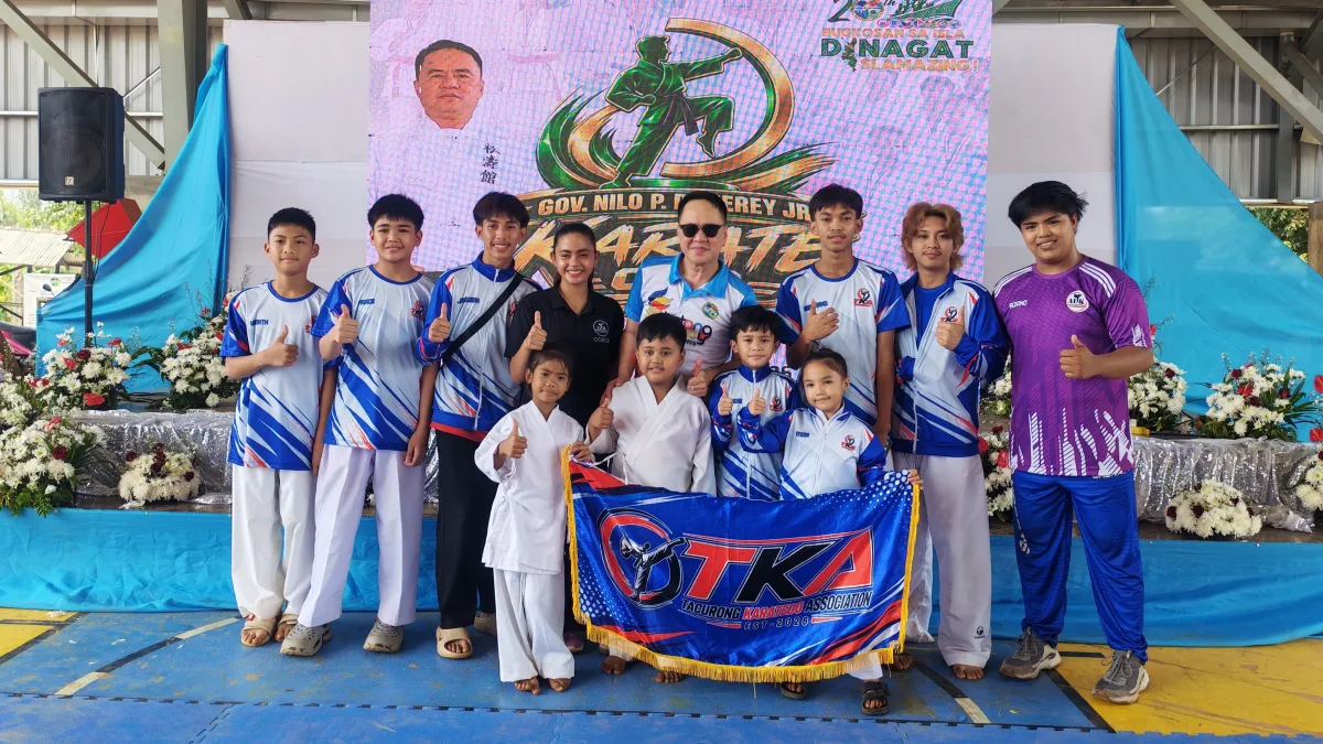 Members and coaches of the Tacurong Karatedo Association (TKA) pose together on stage holding their organizational banner during the 4th Governor Nilo P. Demerey Jr. Karate Cup 2026 at the Provincial Capitol Dome in Dinagat Islands.