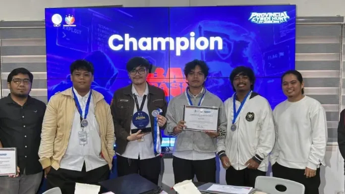 Members of Western Mindanao State University's Team BaiPass pose on stage holding their certificates, trophy, and medals alongside event organizers in front of a digital display that reads "Champion" and "BaiPass".
