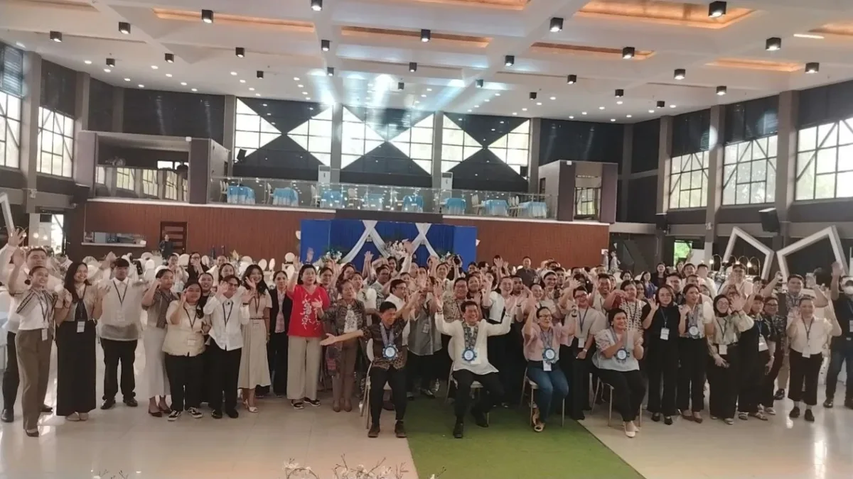 Attendees, healthcare leaders, and students wave and cheer during a group photo at the 9th Regional Health Research Conference at D’Orchard Hall in Iligan City.
