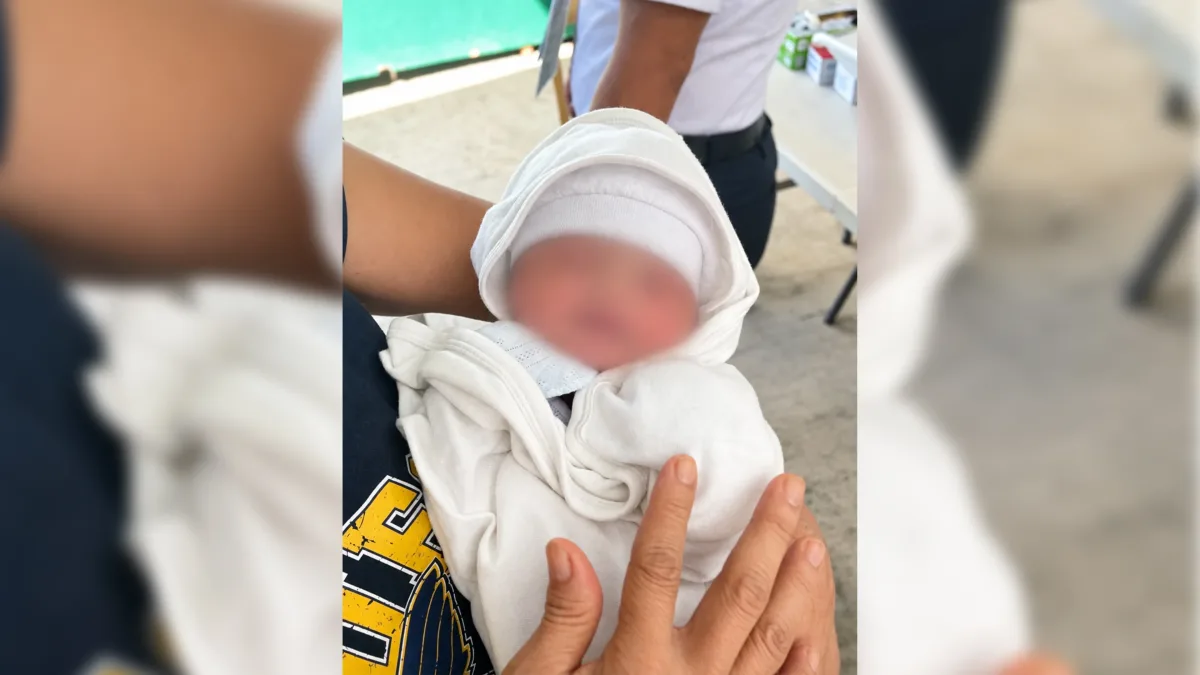 A newborn girl wrapped in a white blanket and cap, named Aurora Hope Medina, is held securely by a care worker following her rescue at a local cemetery in Medina, Misamis Oriental.