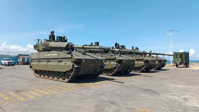 Four Philippine Army ASCOD II Sabrah light tanks stand lined up on a tarmac near the coast, with the lead tank bearing the name "CPT ROMMEL B SANDOVAL" stenciled on its hull.