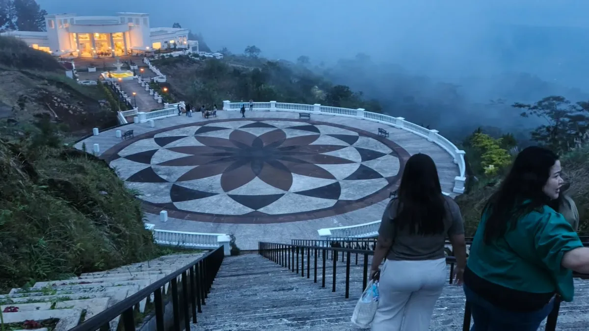 Visitors walk down stone stairs leading to a large geometric star-patterned observation plaza overlooking fog-shrouded mountain slopes and illuminated white structures at Asenso Global Gardens in Tangub City, Misamis Occidental.