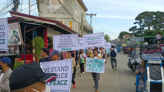 Bangsamoro religious leaders, youth, women, and civil society advocates march through a street in Marawi City holding peace placards urging the implementation of the Comprehensive Agreement on the Bangsamoro.