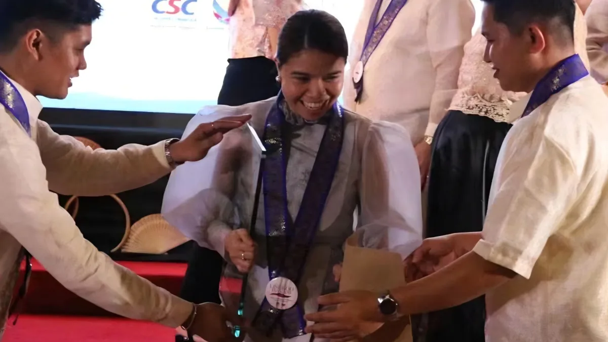 Xsyclyn Faith "Kanzai" B. Lumbatan smiling as she receives the CSC PRIME-HRM Bronze Award plaque on stage during the CSC Region 10 awarding ceremony.
