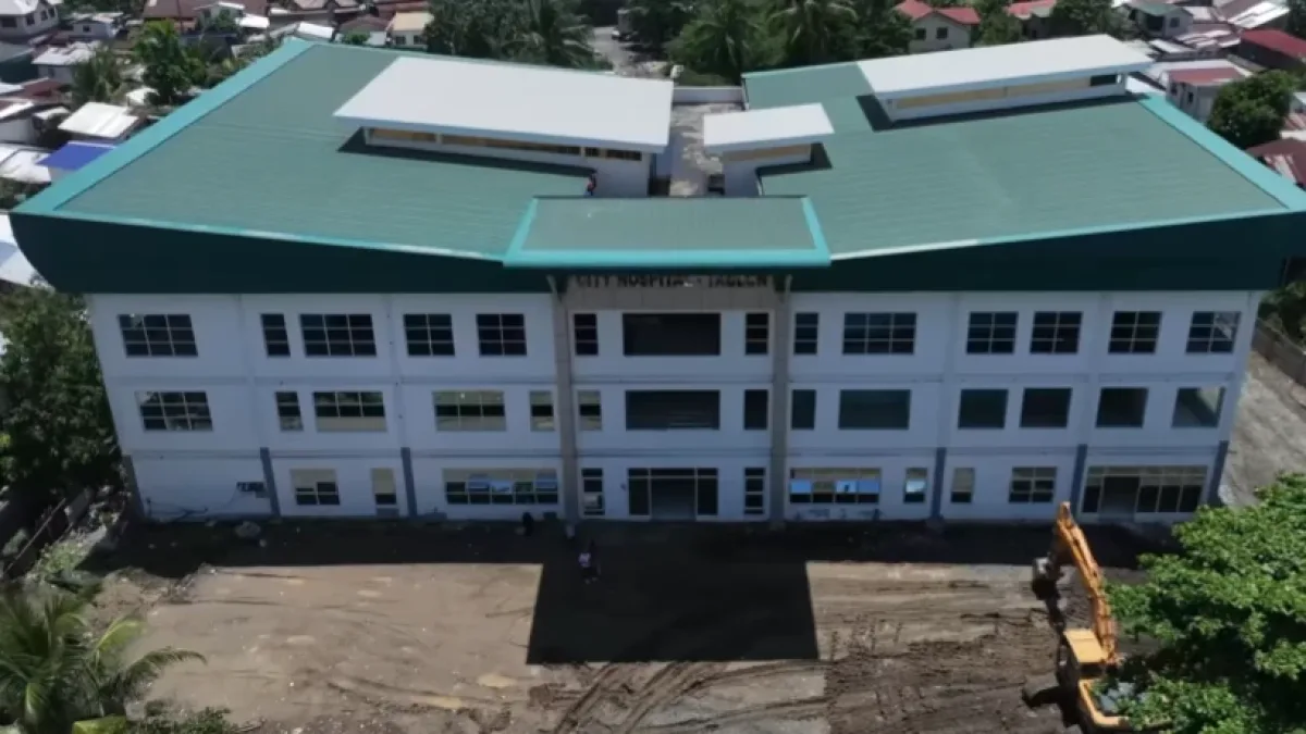An aerial view showing the newly constructed multi-story City Hospital in Barangay Tablon, Cagayan de Oro City, surrounded by residential structures and construction equipment.