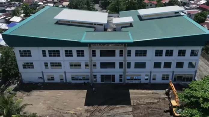 An aerial view showing the newly constructed multi-story City Hospital in Barangay Tablon, Cagayan de Oro City, surrounded by residential structures and construction equipment.
