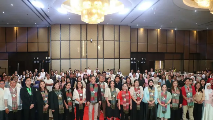 CoScho scholars, program graduates, and organizers wearing woven ceremonial sashes pose for a group photo inside a decorated hotel ballroom during the inaugural regional Scholars’ Summit in Cagayan de Oro City.