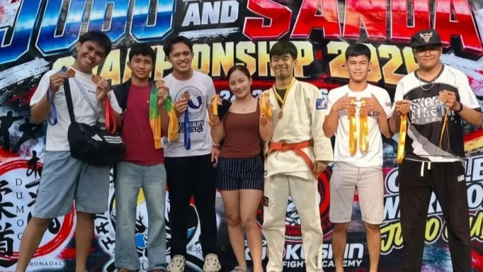 Athletes and coaches from Davao City's Gentle Warrior Judo Club display their medals in front of the tournament backdrop at the 2nd South Central Mindanao Judo and Wushu Sanda Championship in Tacurong City.