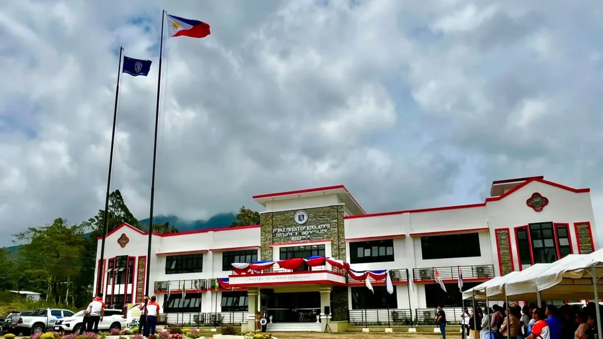 An exterior view of the newly constructed two-storey DepEd Gingoog City Division Office building with bunting decorations, flagpole, and attendees gathered under tents during the blessing ceremony.