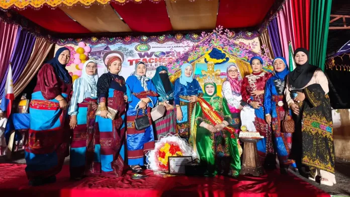 Dr. Raquelina Aguam Benito, seated in a green royal attire with a sash, poses on stage alongside educational leaders and guests during the World Teachers' Day celebration in Lanao del Sur.