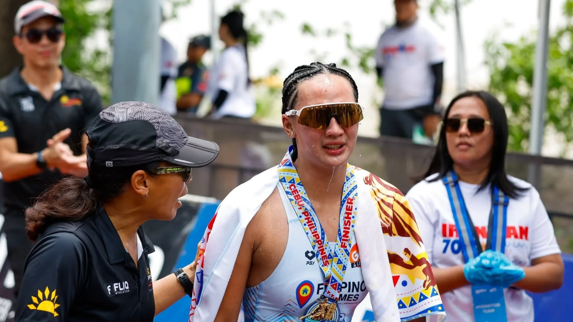 Triathlete Ellaiza Nicole Rojo wears a finisher medal and towel over her shoulders as a support crew member assists her immediately after crossing the finish line at Ironman 70.3 Lapu-Lapu in Cebu.