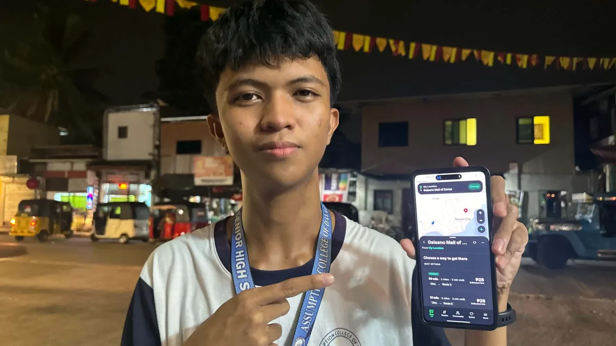 Seventeen-year-old Grade 12 student Francisco Navalta, wearing an Assumption College of Davao lanyard, holds up his smartphone displaying the interface of his DavaoGo transit navigation application.