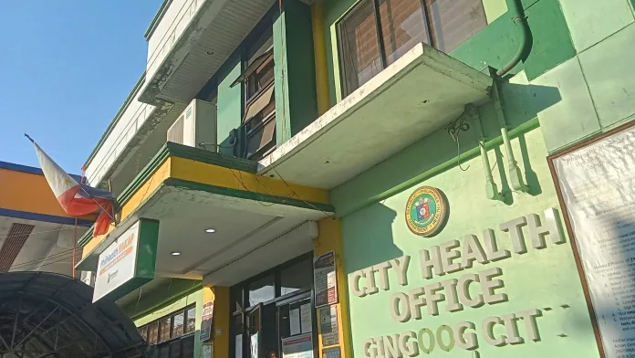 The exterior facade of the Gingoog City Health Office building in Misamis Oriental, featuring green and yellow walls, official Department of Health signage, and a PhilHealth program board.