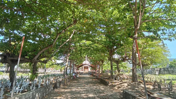 A tree-lined paved walkway leading toward a central chapel structure at the Roman Catholic Cemetery in Gingoog City, Misamis Oriental, ahead of Undas 2026.