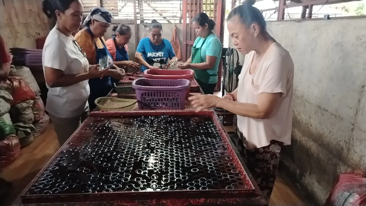 Members of GSK work around a candle molding table during a community livelihood training project, filling molds to manufacture candles for supplementary income.