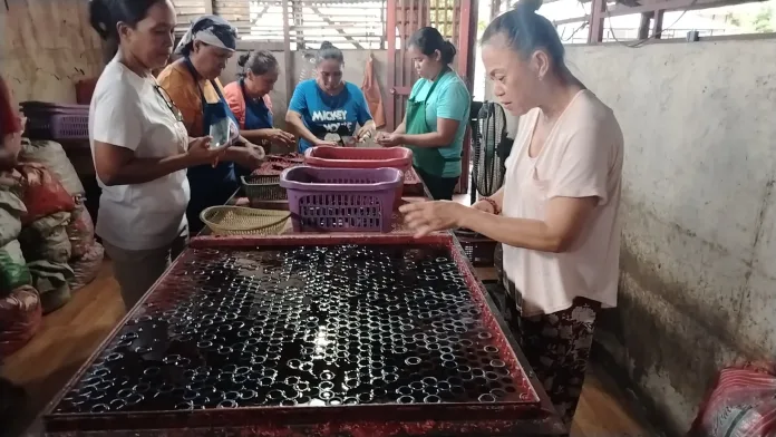 Members of GSK work around a candle molding table during a community livelihood training project, filling molds to manufacture candles for supplementary income.