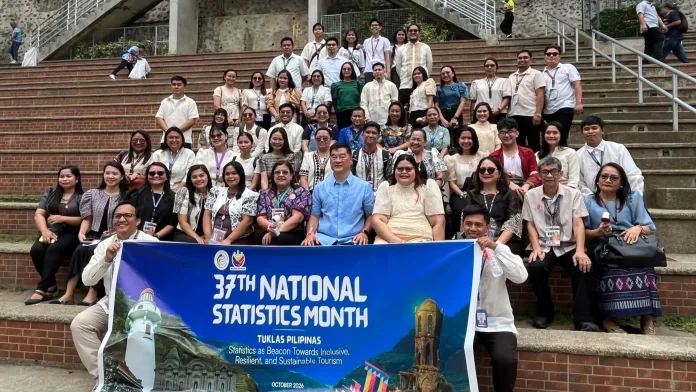 City officials, PSA representatives, and event delegates display the 37th National Statistics Month banner while sitting on outdoor stone steps in Iligan City.