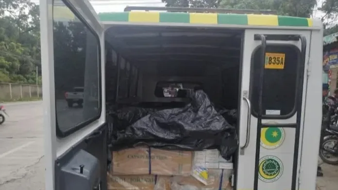The open rear cargo doors of a white utility vehicle reveal master cases of confiscated Cannon cigarettes covered by a black tarp during a police highway checkpoint intercept in Iligan City.