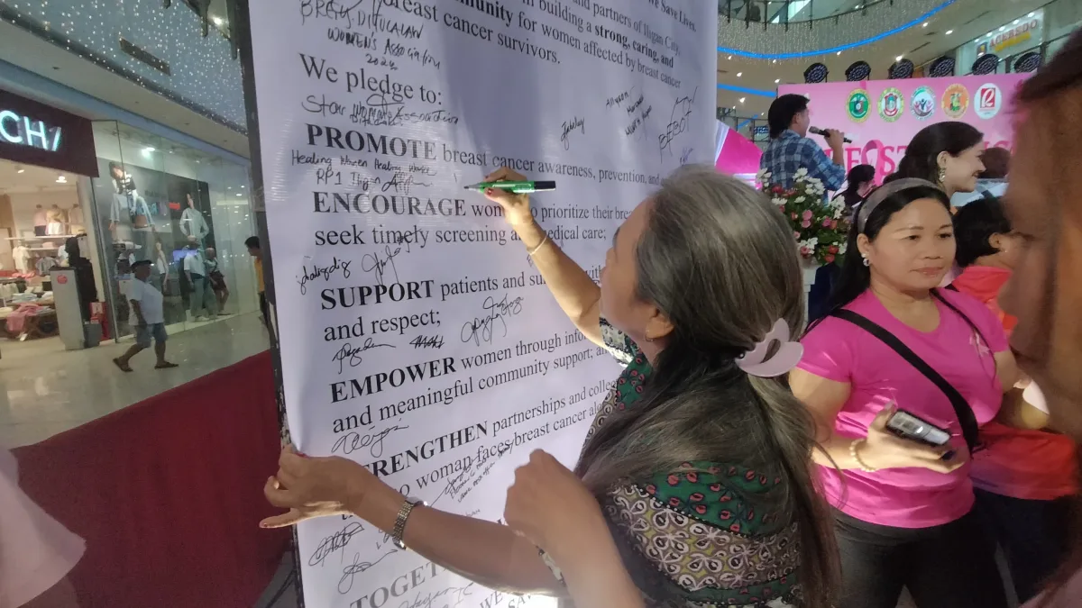 Participants and advocates sign a large commitment pledge board promoting breast cancer awareness, early screening, and community support during Breast Cancer Awareness Month at Robinsons Atrium in Iligan City.