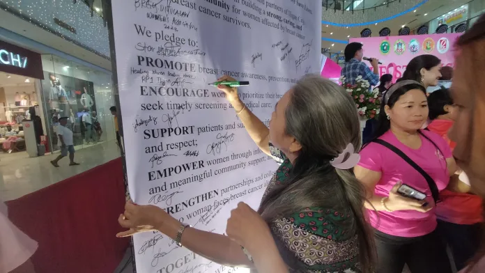 Participants and advocates sign a large commitment pledge board promoting breast cancer awareness, early screening, and community support during Breast Cancer Awareness Month at Robinsons Atrium in Iligan City.